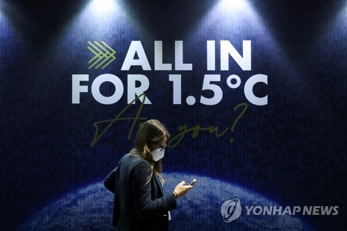 영국 글래스고에서 2021sus 11월에 열린 제26차 유엔 기후변화협약 당사국총회 회의장에서 한 참석자가 '기온 상승을 섭씨 1.5도로 억제하는데 모두 힘을 합치자'는 내용의 슬로건 앞으로 지나고 있다. 로이터=연합