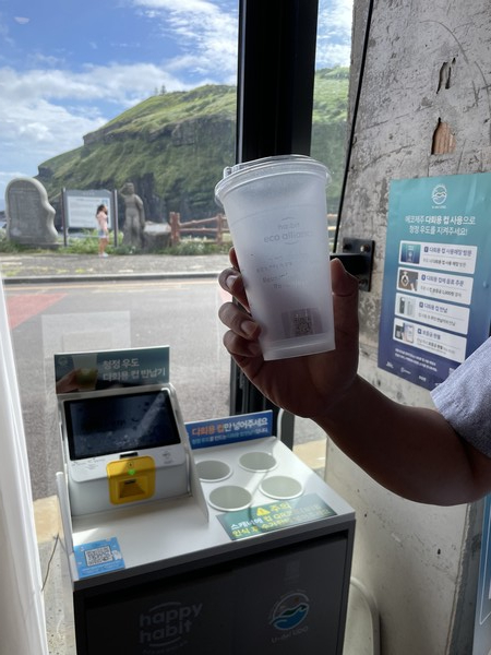 제주시 우도면 검멀레 해변가 한 카페에 있는 다회용컵반납기 앞에서 카페 매니저가 다회용컵을 들어보이고 있다. 이 컵을 반환하면 1000의 현금이나 1100원의 포인트를 적립할 수 있다. 사진=ESG경제