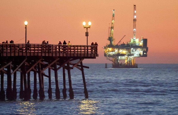 2025년 1월 5일 캘리포니아주 씰 비치(Seal Beach)에서 사람들이 해상 석유 및 가스 시추 설비가 보이는 부두에 서 있다. AFP=게티=연합